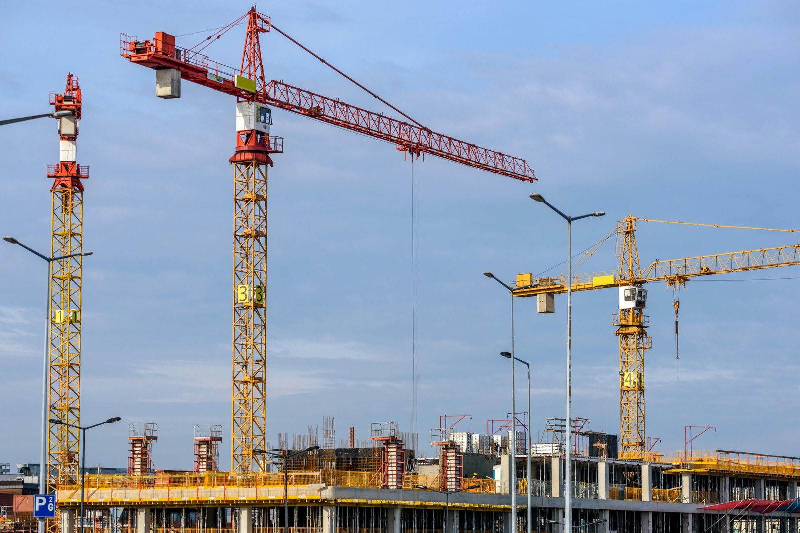 Índice Nacional da Construção Civil varia 0,88% em junho 1 Multiple tower cranes working on a large construction site with blue sky backdrop.